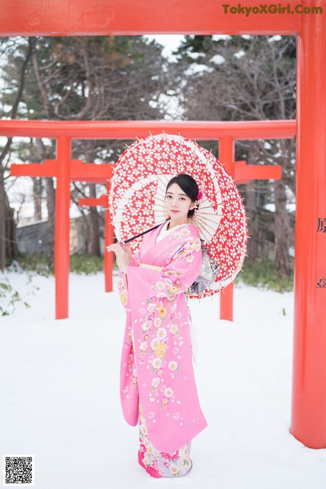 A woman in a pink kimono holding an umbrella in the snow.