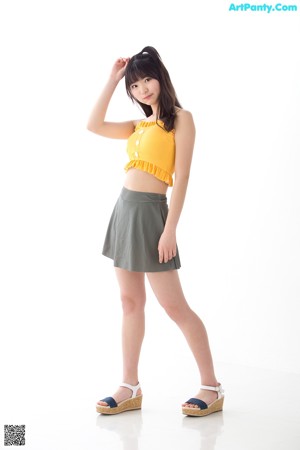 A woman standing in front of a white wall wearing a yellow top.