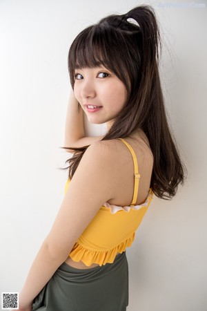 A woman in a yellow top and gray skirt posing for a picture.