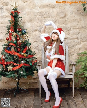 A woman in a santa claus outfit sitting in front of a Christmas tree.