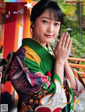 A woman in a colorful kimono standing in front of a gate.