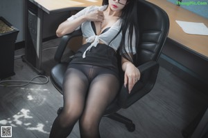 A woman in a black lingerie sitting on a black couch.